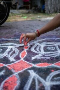 Woman drawing a Margazhi kolam on the ground at the entrance